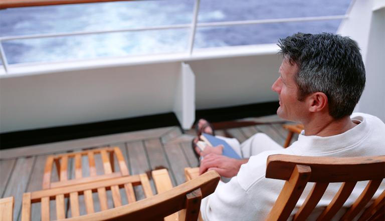 a man on the deck of a cruise ship with a book in his lap