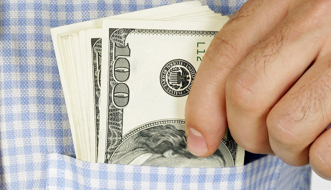 Close Up Of A Man's Hands Putting Wads Of 100 US Dollar Bills In His Shirt Pocket, How To Avoid Hidden Costs On Cruises