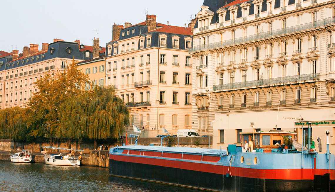 A River Boat Sits In The River And Canal Flanked With Streets And Buildings In A European City, European River Boating