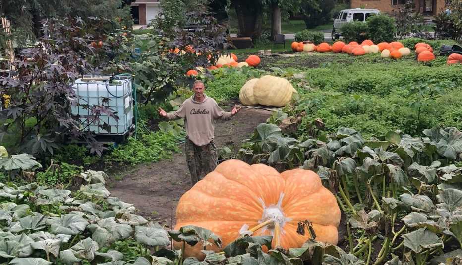 man standing in a pumpkin field next to a giant pumpkin