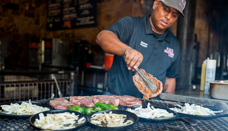 a man cooks meat on a grill at hard eight barbecue in the colony texas