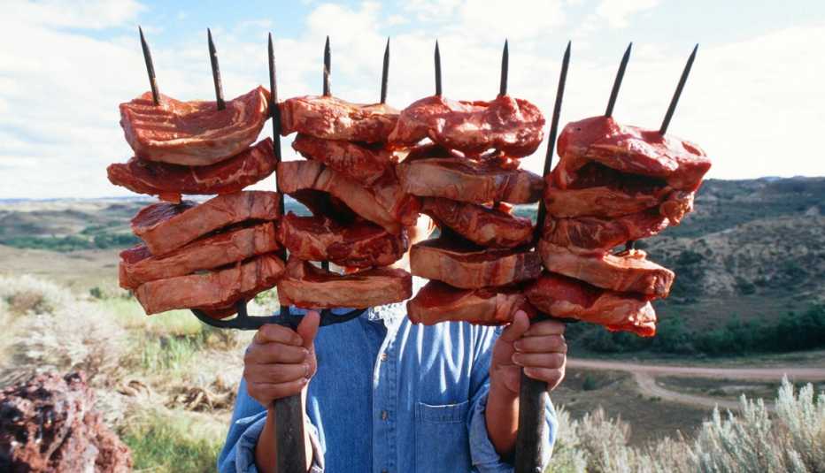 a man holding two pitchforks with raw steaks on the tines