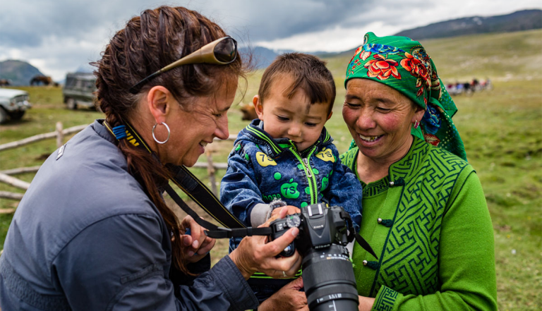 a woman on a photo tour in mongolia shows a young boy and his mother a picture she took of them