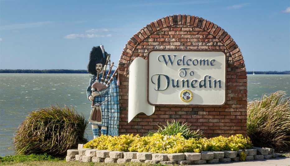 statue of man with bag pipes standing next to the Welcome to Dunedin sign 