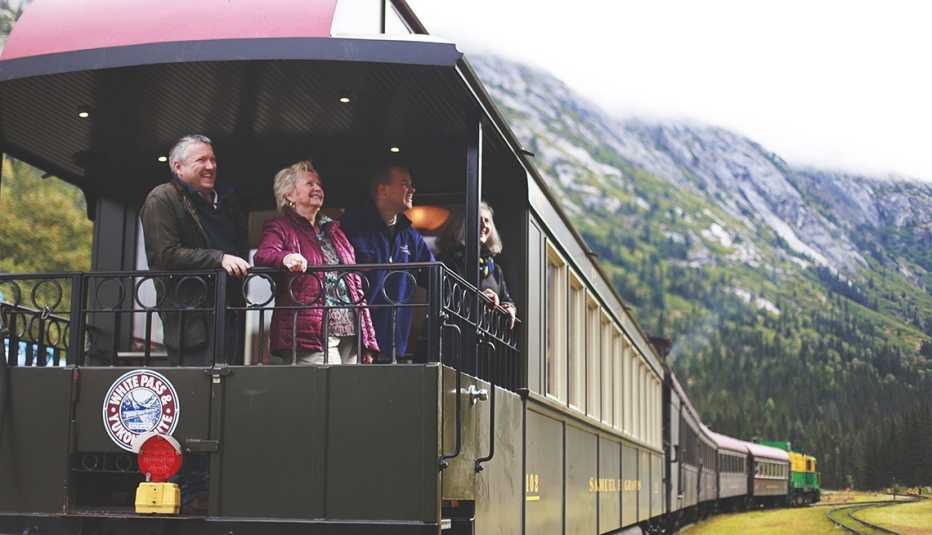 passengers stand on the outdoor caboose of the train on the white pass and yukon route in alaska