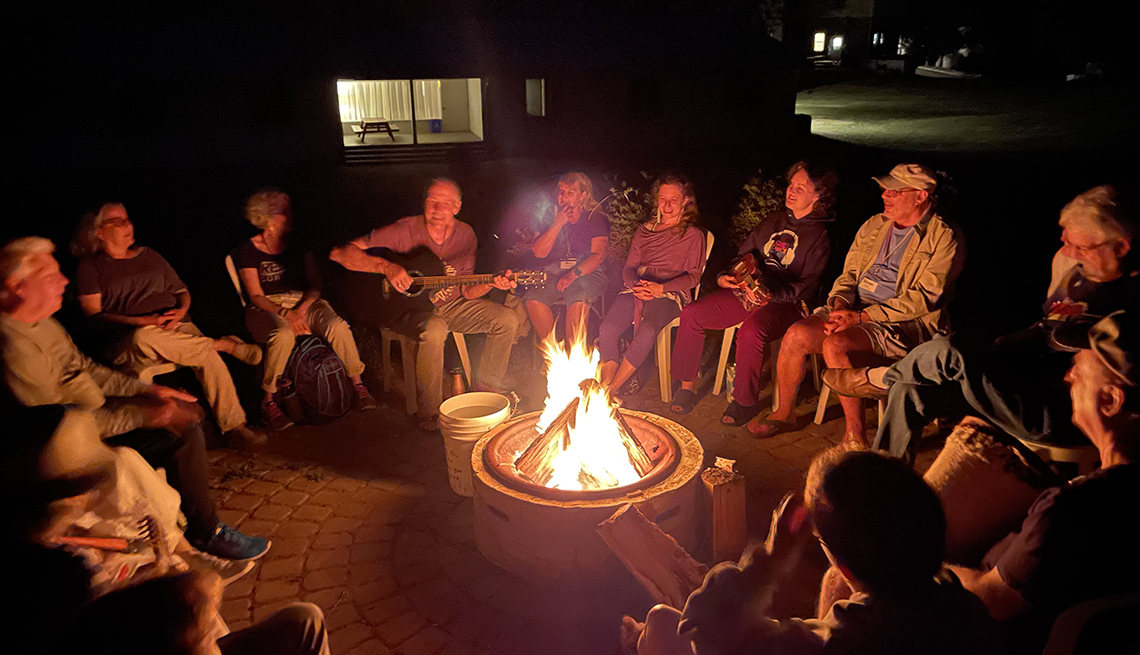 gathering of adults around a campfire singing and playing instruments