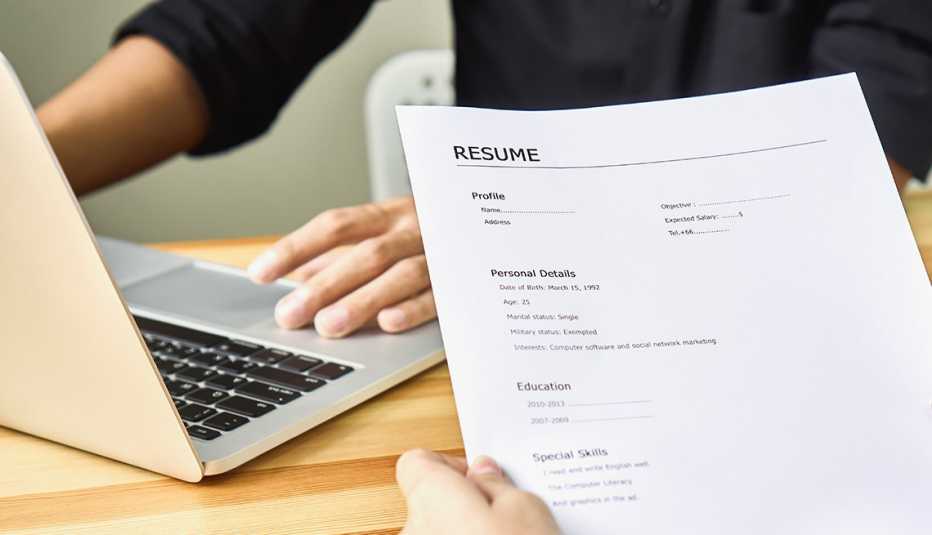 person holds a resume in front of a laptop