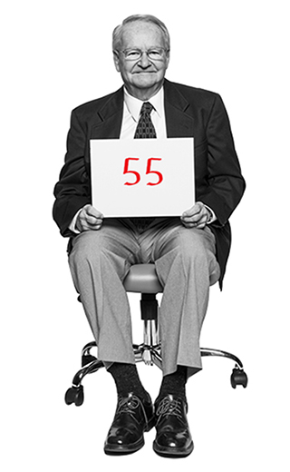Jack Gross holds a placard with the number 55 written on it in red marker sits in an office chair