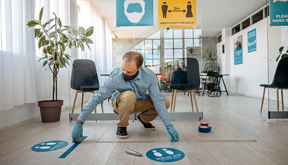 man getting an office space ready for staff return by putting distancing spots on the floor