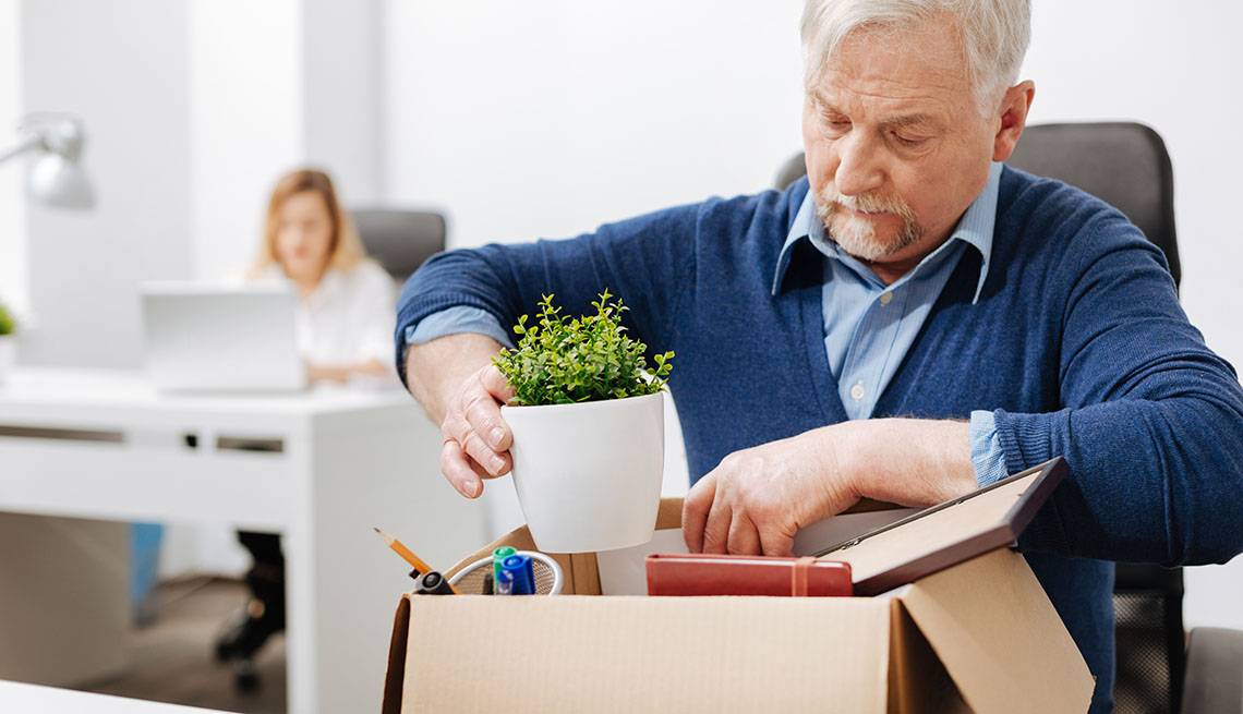 Older office manager sitting in the office and gathering his belongings while holding the box and expressing despair