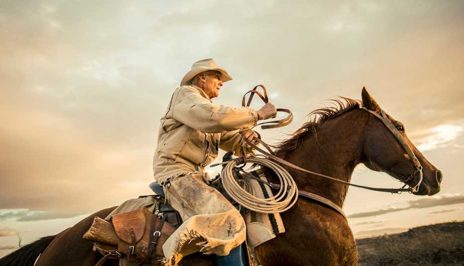 a man dressed for working on a ranch rides a horse against a pretty sky background