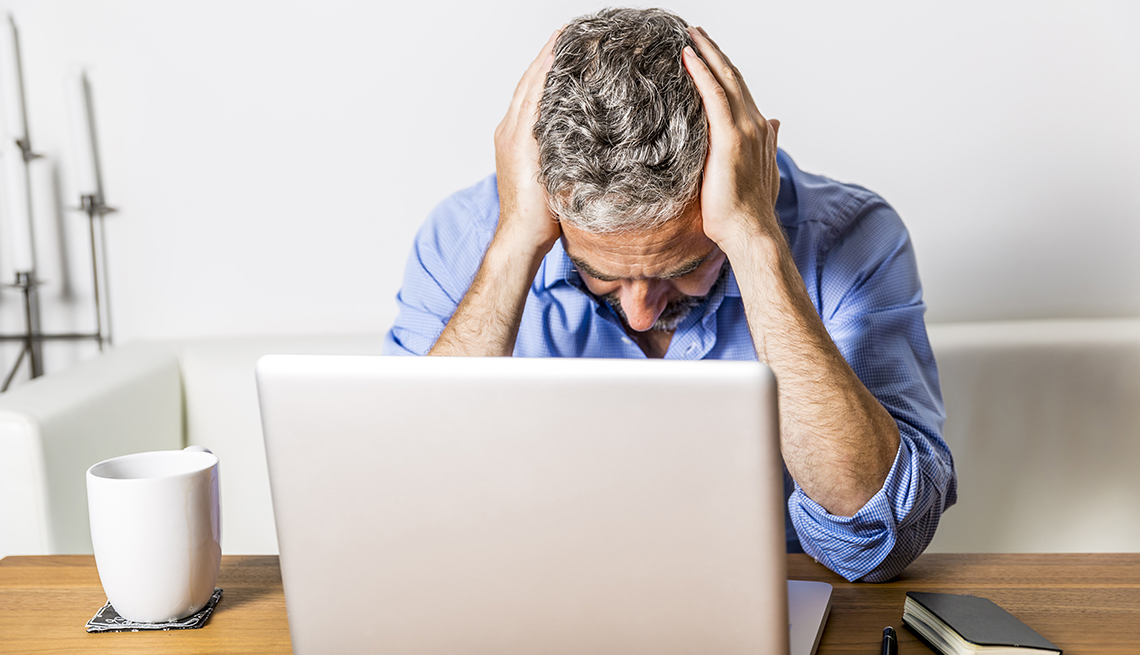 a man in front of a laptop holds his head in his hands
