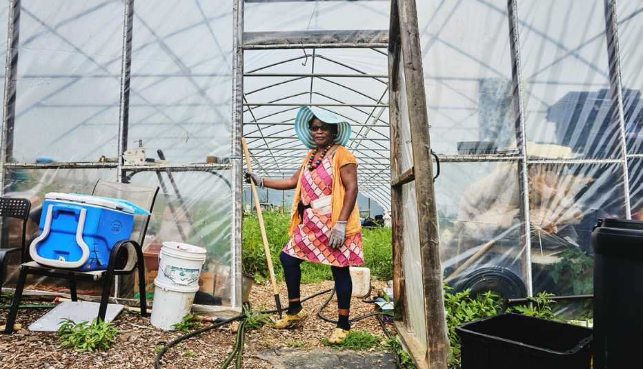 tanya doka-spandhla wears a coloful dress while she stands in a greenhouse doorway with a gardening tool