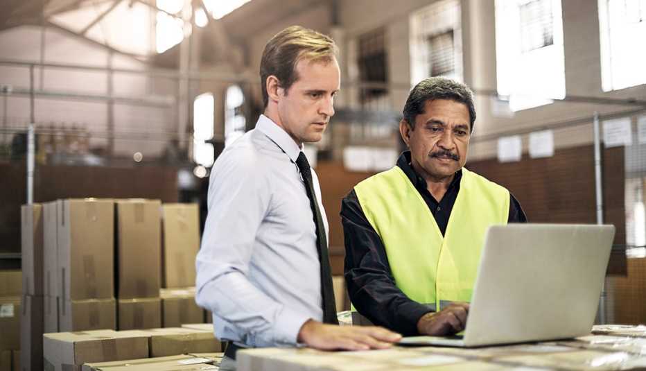 a man in a white shirt and tie and a man in a yellow safety vest look at a laptop