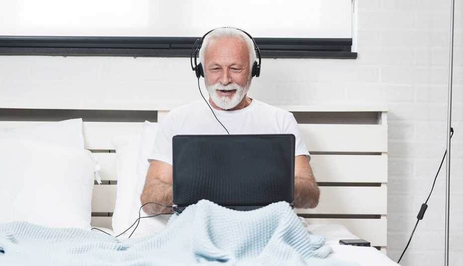 A man is sitting in bed with headphones and a computer