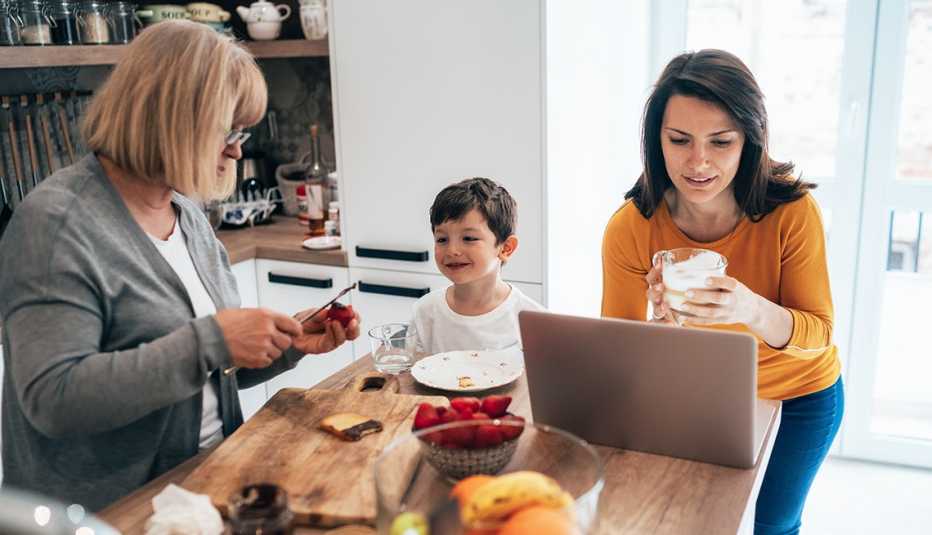 Woman working at home on a laptop next to her young son and mother