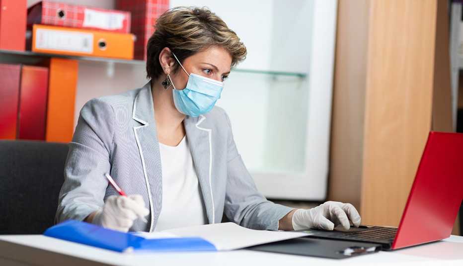 woman at work using a laptop in her office while wearing a facemask