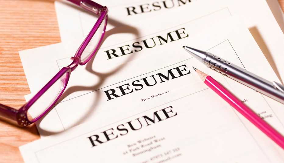 a stack of resumes under a pair of glasses, a pen and a pencil