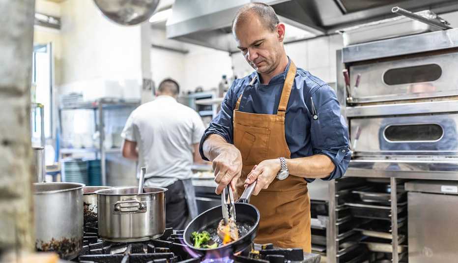 A chef cooks steak with fresh vegetable in a pan at a restaurant kitchen