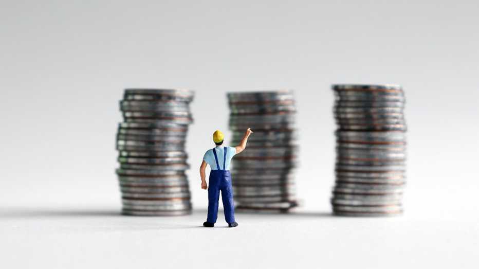 a miniature man in a construction worker outfit points at stacks of coins