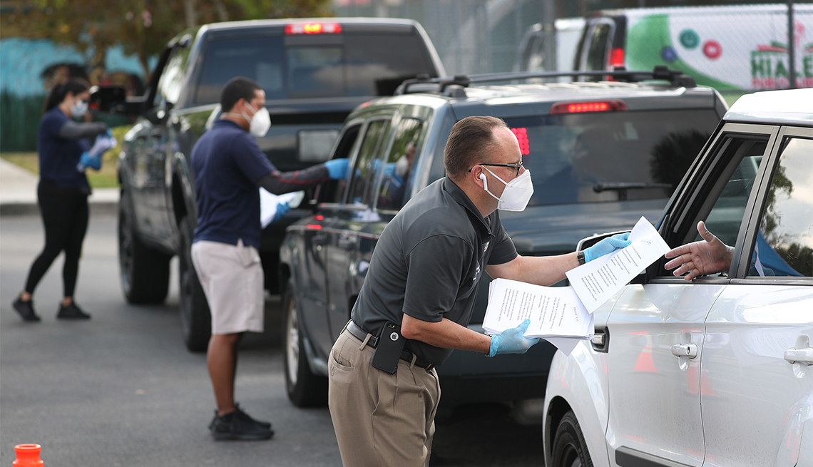 Eddie Rodriguez (R) and other City of Hialeah employees hand out unemployment applications to people in their vehicles 