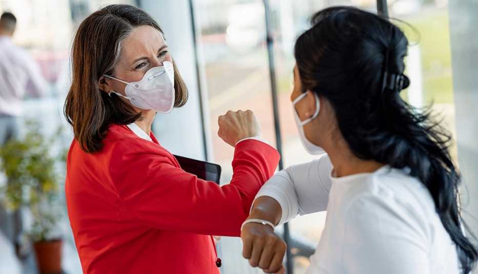 two business women touch elbows while wearing masks