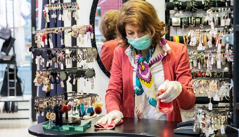 A woman is cleaning the counter of her store while wearing a mask and gloves