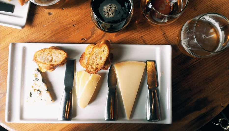 Vista desde arriba de un plato con rebanadas de queso y pan y vasos con cerveza
