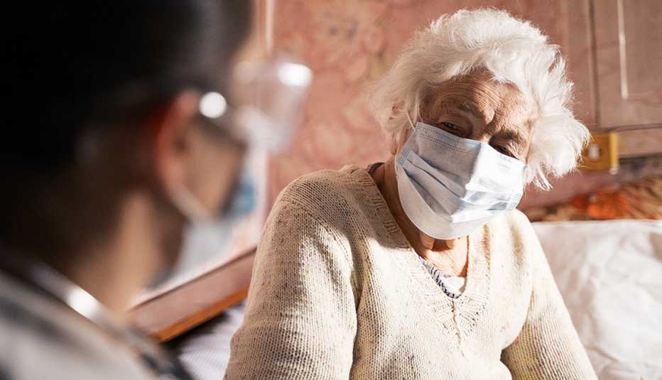   Doctora con EPP se sienta frente a un paciente con una mascarilla