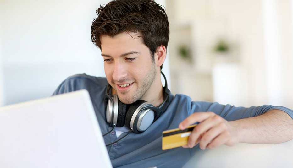 Hombre joven frente a una computadora portátil y con una tarjeta de crédito en la mano