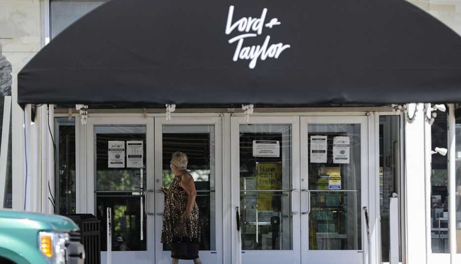 Mujer frente a la entrada de la tienda por departamentos Lord & Taylor donde ve un anuncio de bancarrota por la pandemia.