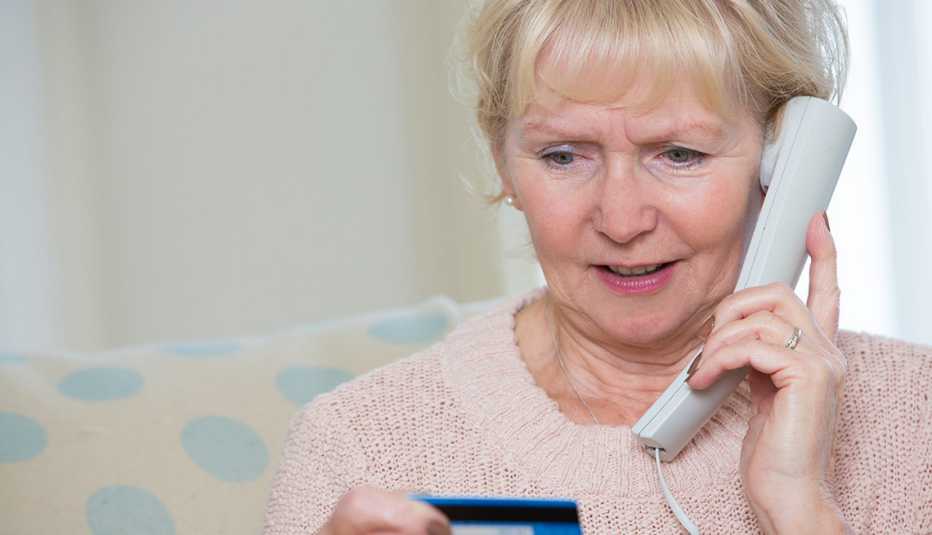 Mujer mayor hablando por teléfono y mirando una tarjeta de crédito.
