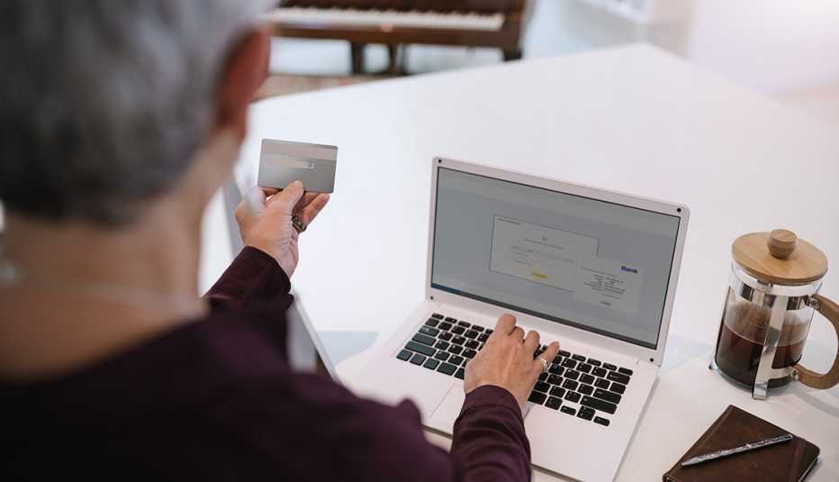 Mujer mayor mirando su tarjeta de crédito y digitando en su computadora personal.