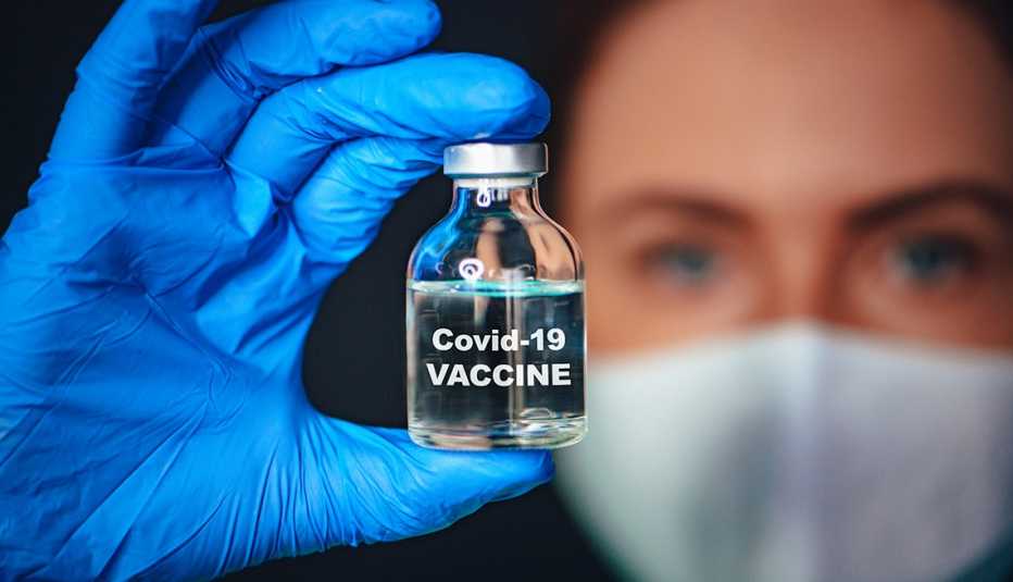 Mujer con mascarilla y guantes sosteniendo una vacuna del coronavirus.