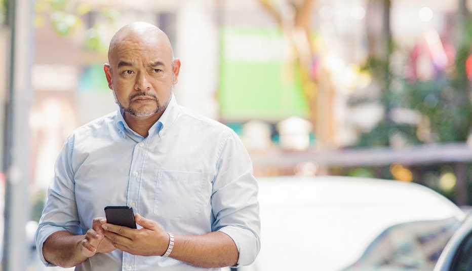 Hombre sostiene un teléfono móvil en la mano mientras mira hacia un lado.