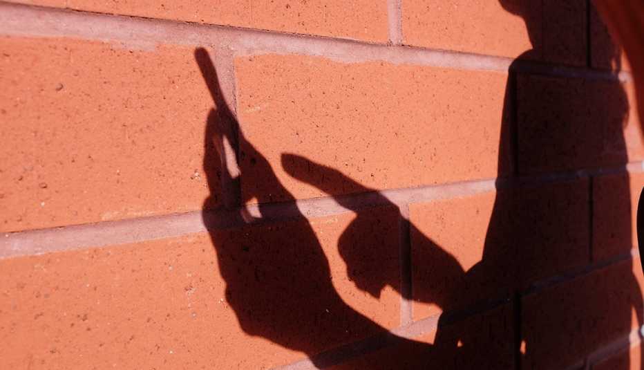 Sombra de una mujer usando un teléfono inteligente sobre un muro de ladrillo