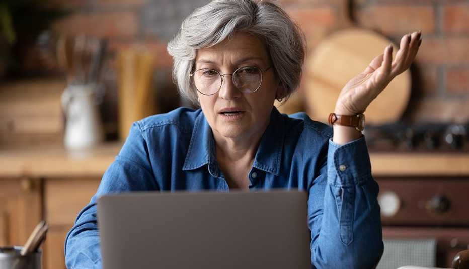 Mujer con gafas sentada frente a su computadora en la cocina de su casa