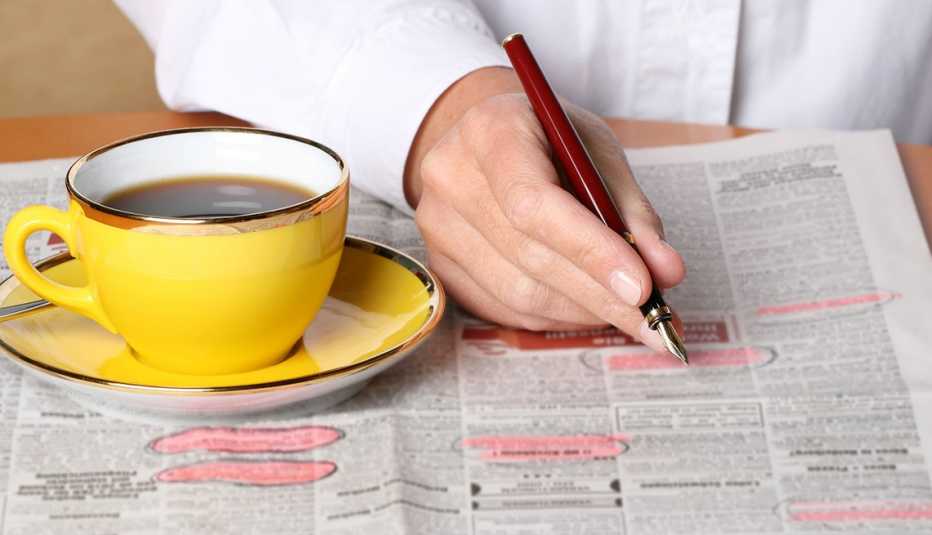 Persona señalando anuncios de trabajo de un periódico con un lapicero y una taza de café al lado