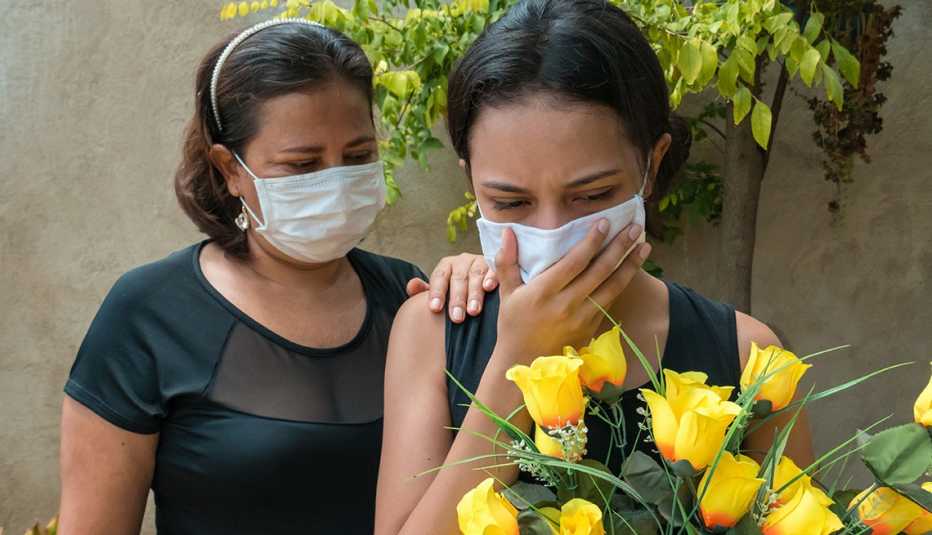 Dos mujeres de luto por la muerte de un familiar, una sostiene flores amarillas.