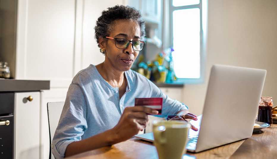Mujer viendo una tarjeta de crédito que sostiene con su mano mientras entra su número en una computadora