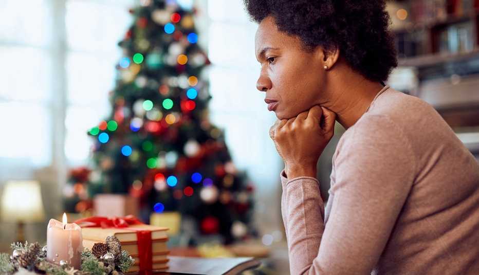 Mujer con cara de preocupación desde su casa decorada con un árbol de navidad en el fondo.