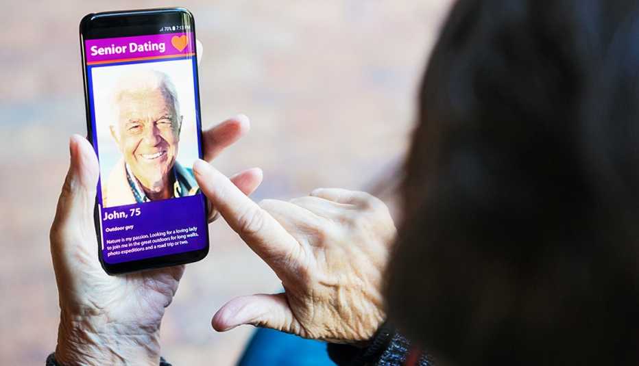 manos de una mujer sostienen un teléfono donde se ve el perfil de un hombre mayor en una aplicación de citas
