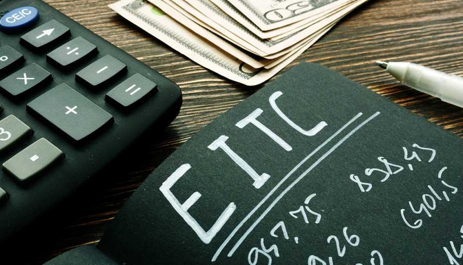 Tablero sobre un escritorio que dice EITC, crédito tributario por ingresos del trabajo, al lado de una calculadora, un lapicero y dinero 