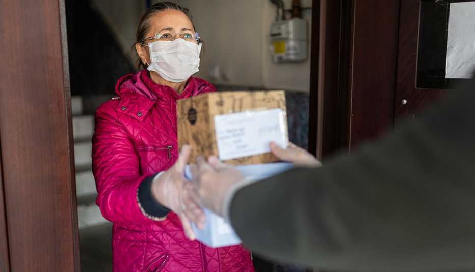 Mujer con guantes y mascarilla devolviendo un paquete a un cartero.