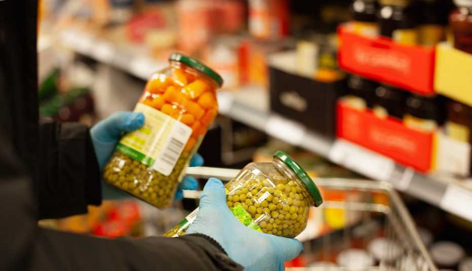 Persona con guantes sosteniendo frascos con conservas en un supermercado.