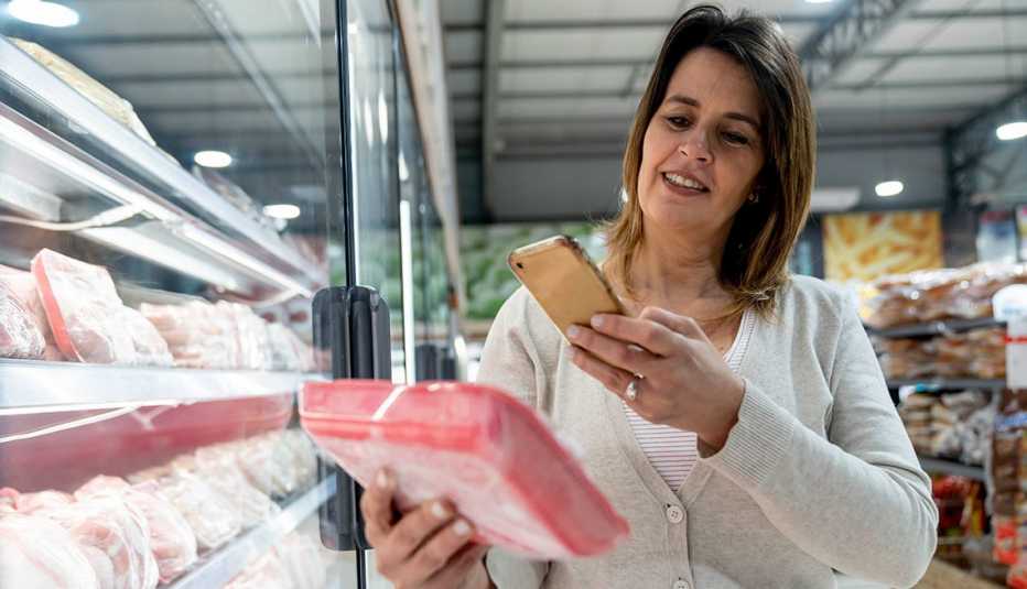 Mujer en un supermercado sostiene un producto y con la otra mano lo escanea con su teléfono.
