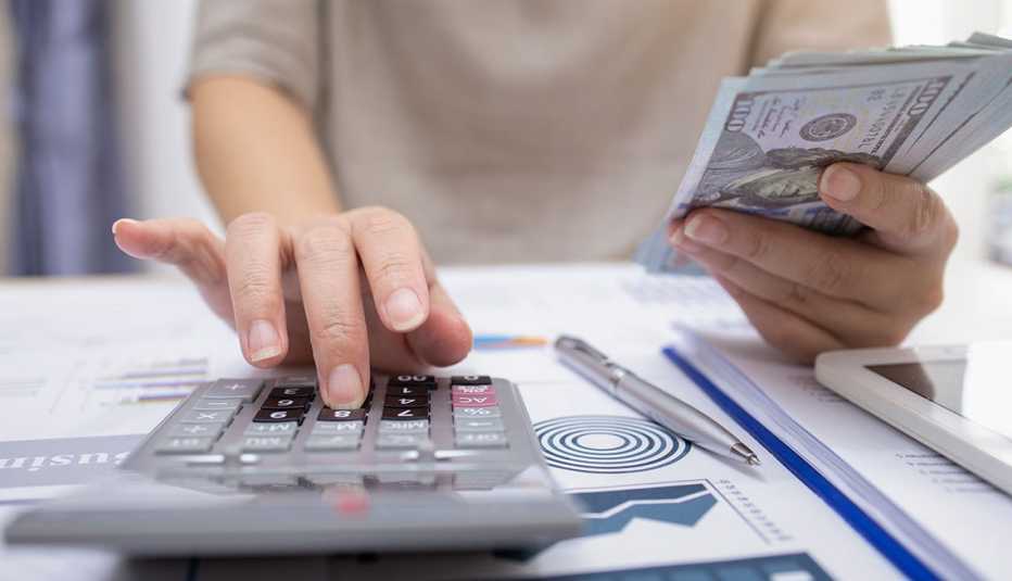 Mujer digitando en una calculadora y sosteniendo un fajo de dólares en la mano.