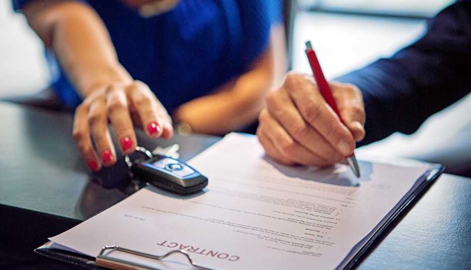 Mano de una mujer a punto de sujetar las llaves de un carro mientras otra mano firma un contrato.