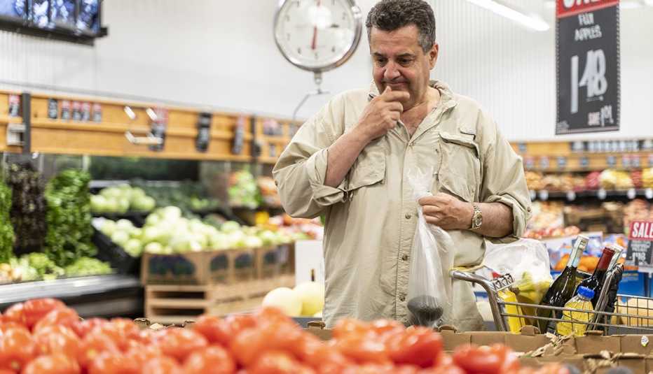 Hombre frente a unos tomates en la sección de vegetales de un supermercado