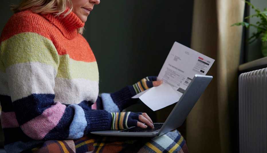 Mujer sostiene una factura de los servicios mientras hace cuentas en la computadora